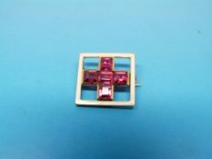 A square yellow metal brooch set with five synthetic rubies surrounded by a square of white enamel