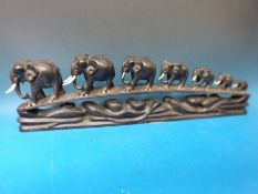 A carved ebony stand featuring a graduated train of elephants with ivory tusks,