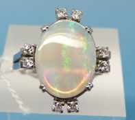 A white metal ring set with a large oval opal and with eight small diamonds set to the sides (size