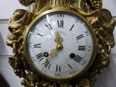 A cast brass French two train wall clock decorated in the Rococo style with goat heads holding