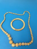 An ivory bangle carved with tigers together with a graduated ivory beaded necklace comprising over