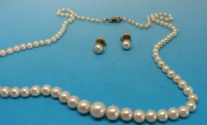 A single strand of pearls with an emerald and diamond clasp together with gold and pearl stud
