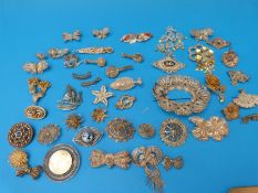 A large collection of white metal filigree brooches including fish, musical instruments,