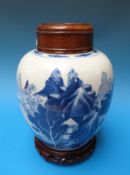 A Chinese blue and white jar with landscape scene with fitted wooden top and stand,