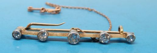 A yellow metal brooch set with five graduating round brilliant cut diamonds,