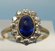 A yellow metal ring set with a sapphire cabochon surrounded by round brilliant cut diamonds (size