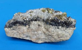A small geological sample formed of light and dark grey crystals on a rock bed,