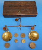 An oak-cased hand-held beam scale with steel beam and brass pans with various coin weights.