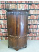 A Georgian oak bow fronted double height corner cupboard,