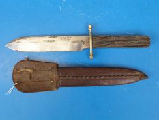 A Bowie knife with antler handle and brass hilt in a leather sheath,