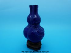 A Chinese blue monochrome double gourd vase with ribbon decoration raised on carved wooden stand