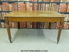 An oak dining or kitchen table raised on turned legs terminating in brass castors (l136 x w90 x