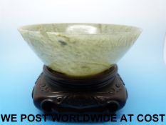A carved Chinese spinach jade bowl on wooden stand,