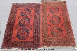 Two similar wool rugs with geometric borders and central lozenge designs on terracotta ground