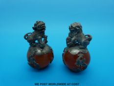 A pair of Chinese white metal mounted amber style balls with dogs to top (6cm tall)
