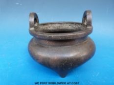 An 18thC/19thC Chinese bronze censer with loop handles and engraved decoration raised on three