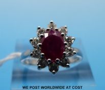 An 18ct white gold ring set with an oval cut ruby surrounded by round brilliant cut diamonds (size