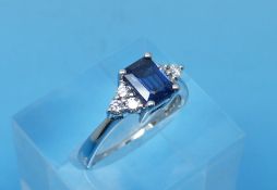 An 18ct white gold ring set with an emerald cut sapphire flanked by three diamonds (size M)