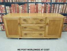 An Ercol light elm sideboard with three drawers flanked by two cupboards (H70 x W156 x D44cm)