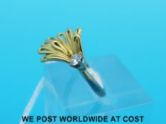 A white metal ring set with a round brilliant cut diamond in a looped yellow metal setting,