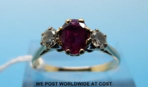 A yellow metal ring set with an oval cut ruby flanked by diamonds (size P)