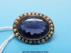 A yellow metal brooch set with a large stone surrounded by seed pearls