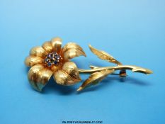 An 18ct gold brooch in the form of a flower with textured surface and a cluster of sapphires to the