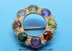 A gold brooch set with eight various gems including emerald and peridot with alternating diamonds