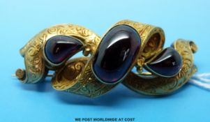A yellow metal brooch in the form of a knot with chased decoration set with three large garnets,
