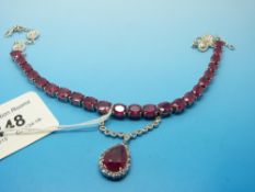 A silver necklace set with 23 oval cut rubies and a drop section set with a large pear cut ruby