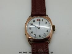 A c1920 gentleman's 9ct gold wristwatch with white enamelled dial in cushion shaped case on brown