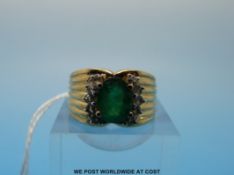 A 9ct gold ring set with an oval cut emerald flanked by five diamonds to each side (emerald