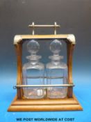 A late 19th / early 20thC oak two bottle tantalus with plated mounts and drop down bar mechanism,