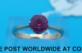 A yellow metal ring set with a round pink sapphire,