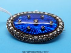 A yellow metal brooch the central blue oval cabochon set with diamonds within a diamond set border
