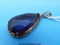 A yellow metal pendant set with a large pearl cut purple sapphire