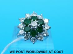 A white metal ring marked 18ct set with a round brilliant cut diamond surrounded by six emeralds,
