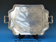 A George V hallmarked silver two handled tray with shaped edge and engraved foliate design raised