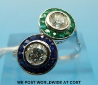 A white gold ring set with two round brilliant cut diamonds one surrounded by emeralds and the