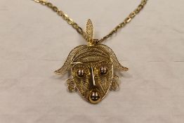 A yellow metal filigree African head brooch, suspended as a pendant upon a flat linked yellow