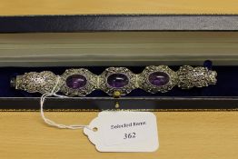 A sterling silver ornate filigree bracelet set with three cabochon amethysts.