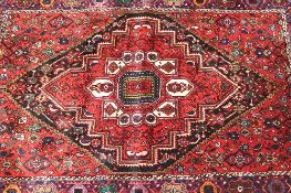 An Iranian wool rug, on red ground, 155 cm x 102 cm.