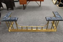 A brass club fender with blue leather upholstery, width 174cm.