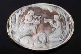 A large oval shell cameo brooch: depicting two maidens serenading a recumbent lion within a plain