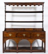 An 18th Century oak dresser:, the shelved superstructure with a moulded cornice and arcaded frieze,