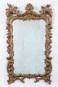 A later gilt decorated cartouche-shaped wall mirror:, the shaped rectangular plate within a foliate,