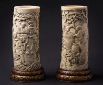 A pair of Japanese carved ivory tusk vases: each decorated with village peasants dancing and making