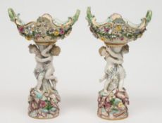 A pair of Meissen table centrepieces: each modelled with a pair of scantily clad cherubs supporting