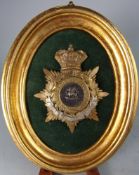A shako badge for the South Wales Borderers: mounted in an oval gilt frame.