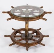 A ship's helm table with circular glass top:, constructed from two helms on a brass column support,